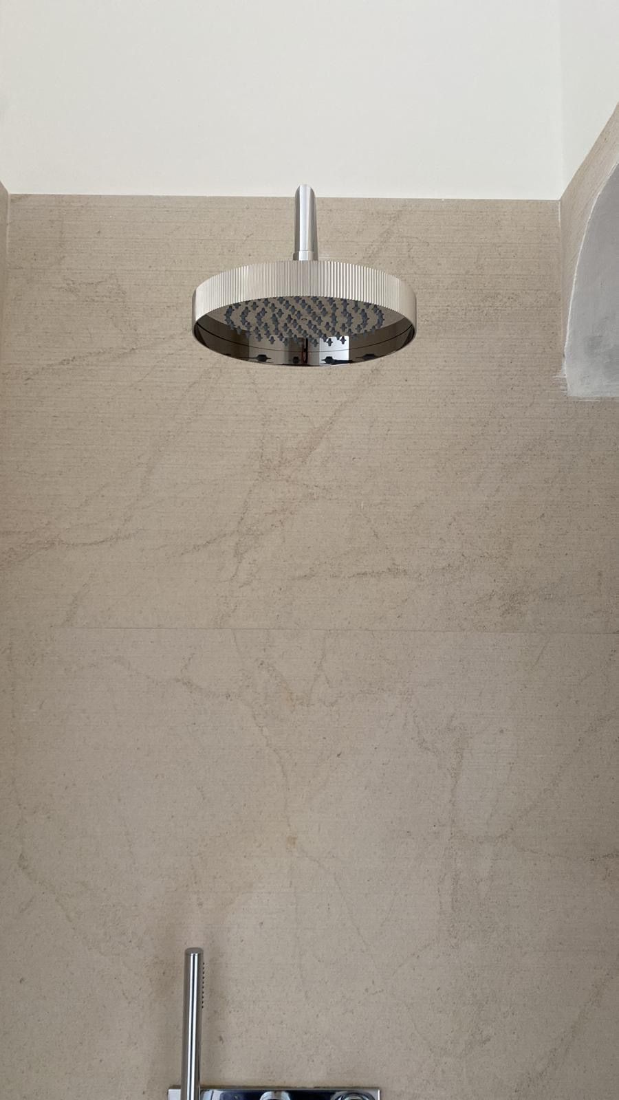 Soffione doccia e rubinetto cromati su una parete del bagno rivestita di piastrelle beige.