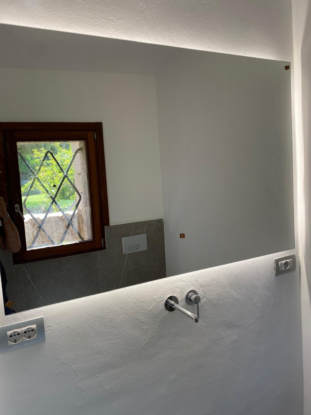Parete del bagno con piccola finestra, specchio e sanitari del lavabo in fase di costruzione.