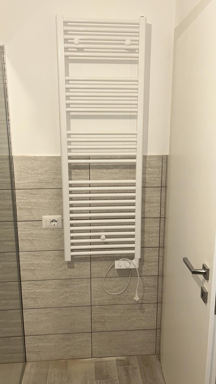 Scaldasalviette bianco a parete in un bagno piastrellato con porta sulla destra.
