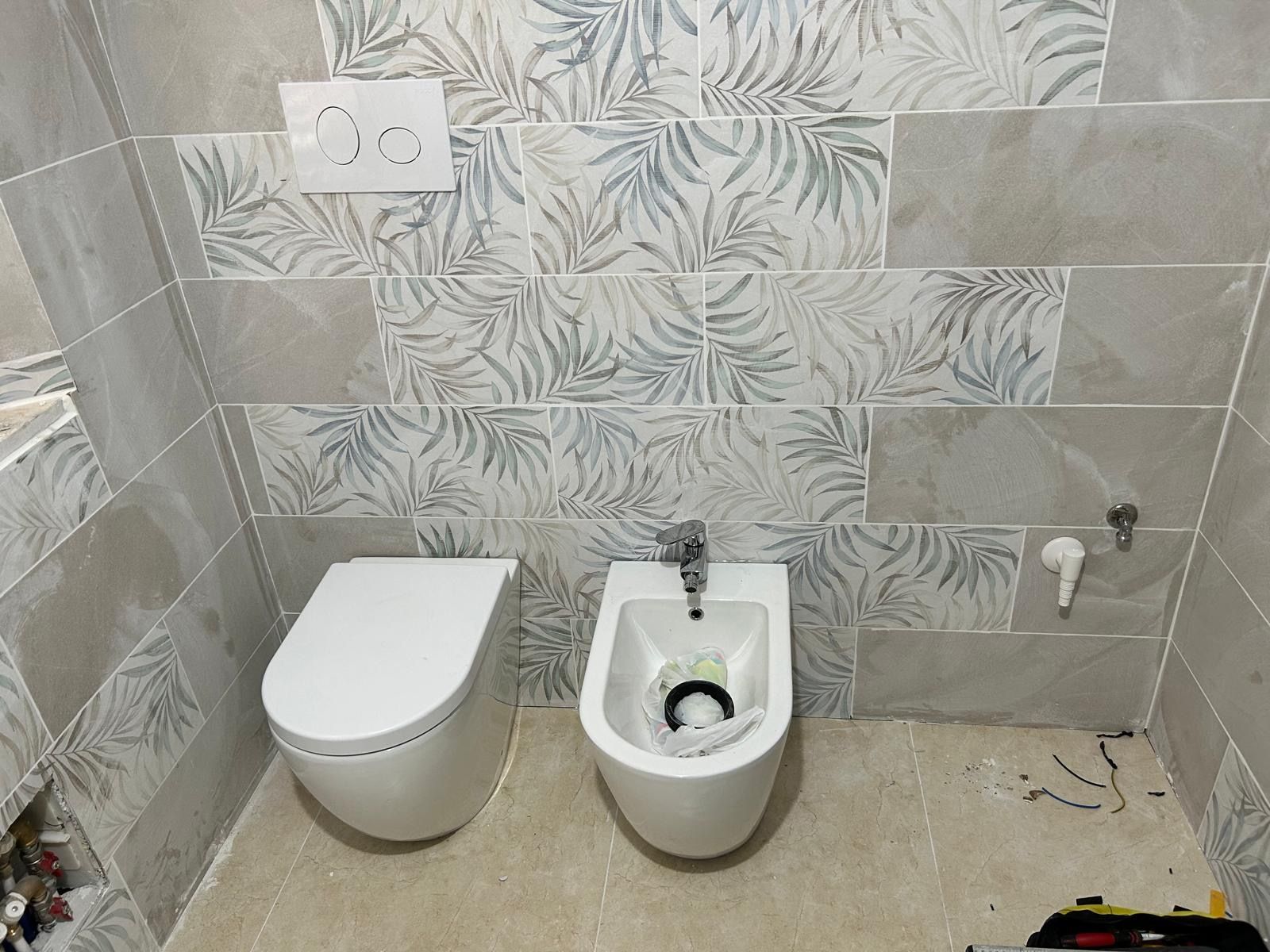 Piccolo bagno piastrellato con WC a parete, bidet e lavabo sulla destra.