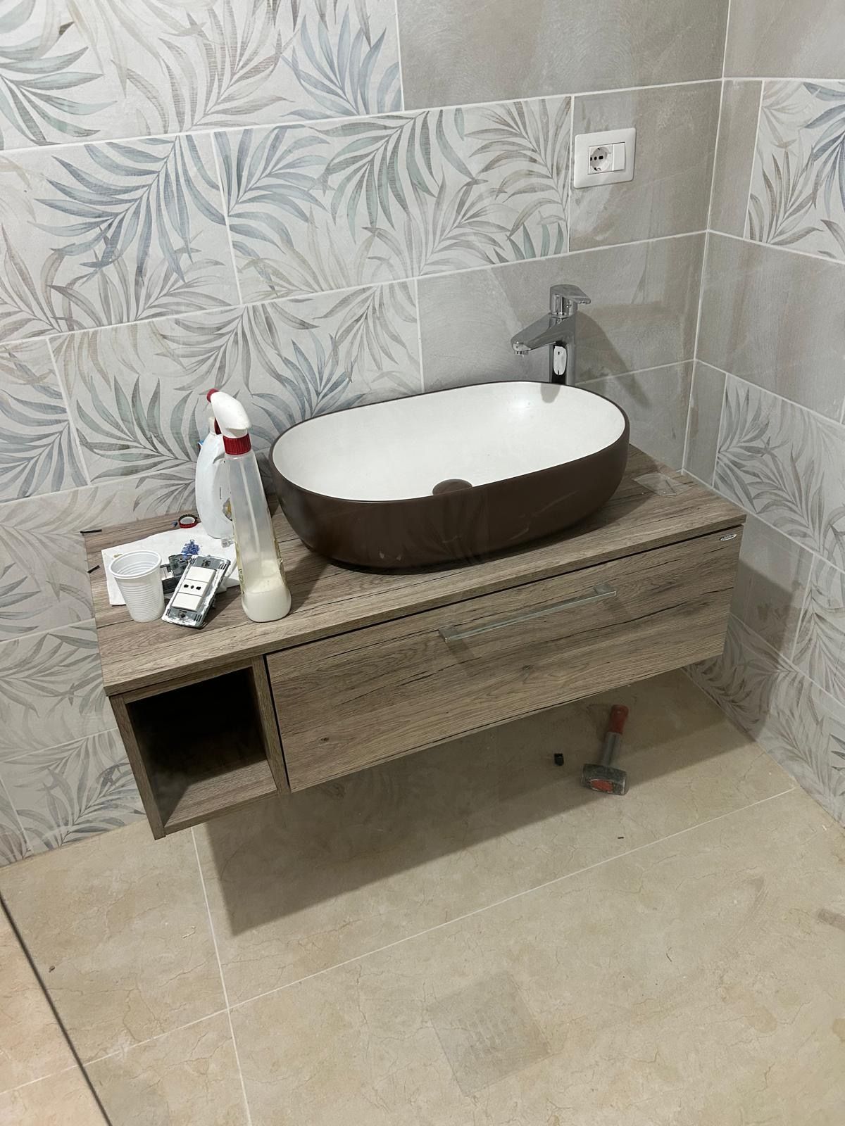 Mobile bagno moderno con lavabo ovale, piano in legno marrone e parete rivestita con piastrelle a motivi floreali.