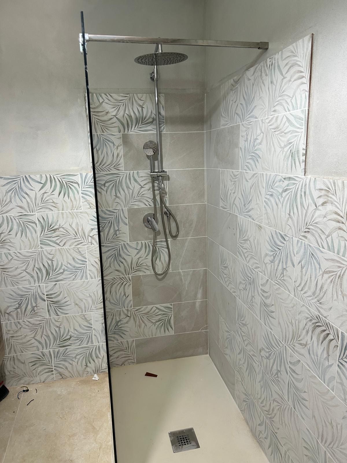 Cabina doccia con pareti rivestite in piastrelle grigie decorate, pavimento bianco e soffione a pioggia cromato.