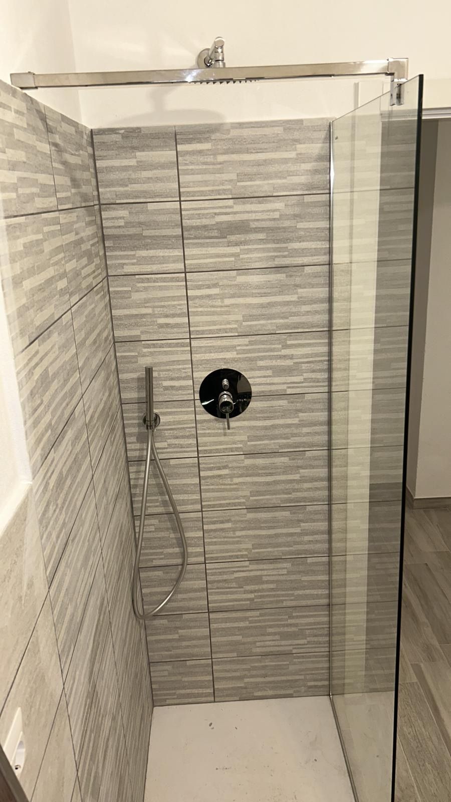 Box doccia piccolo piastrellato con porta in vetro e soffione a parete.