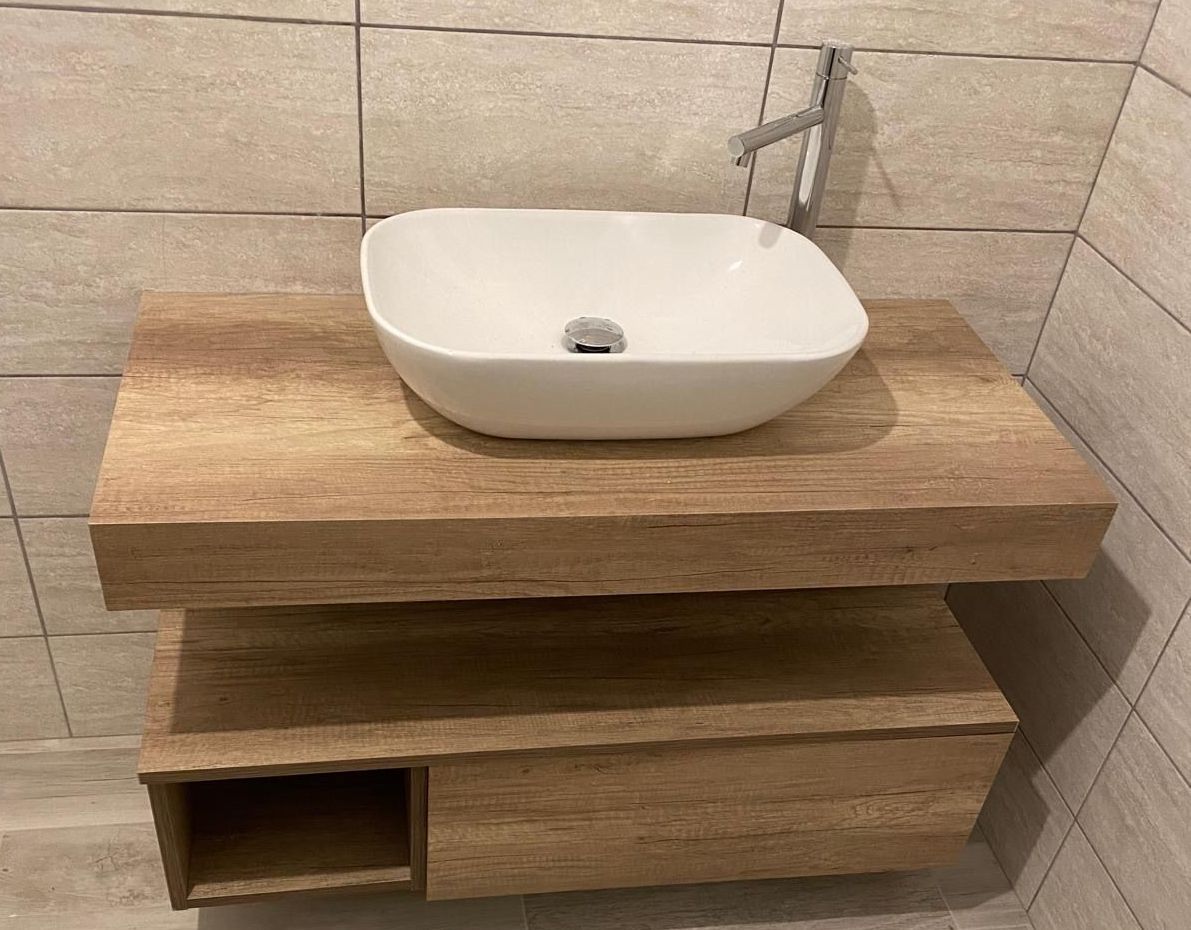 Lavabo moderno su mobiletto in legno con mensola a vista, contro pareti rivestite di piastrelle beige.