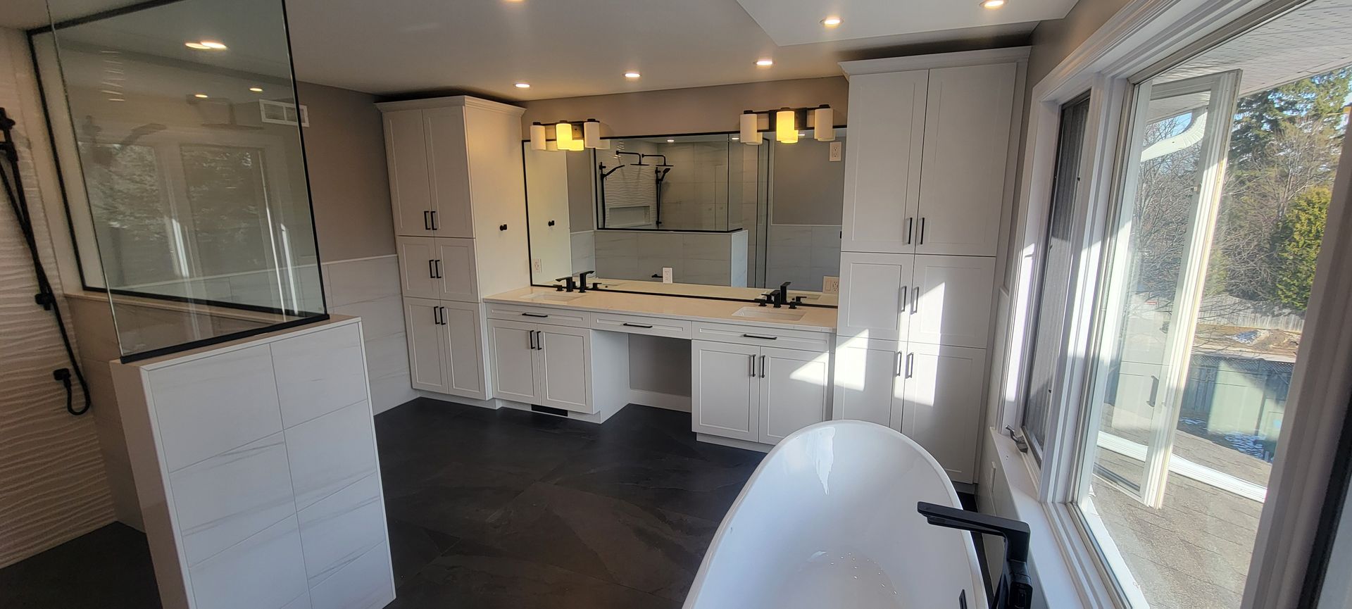 Bright white modern kitchen with dark flooring, large windows, and a bathtub in the foreground