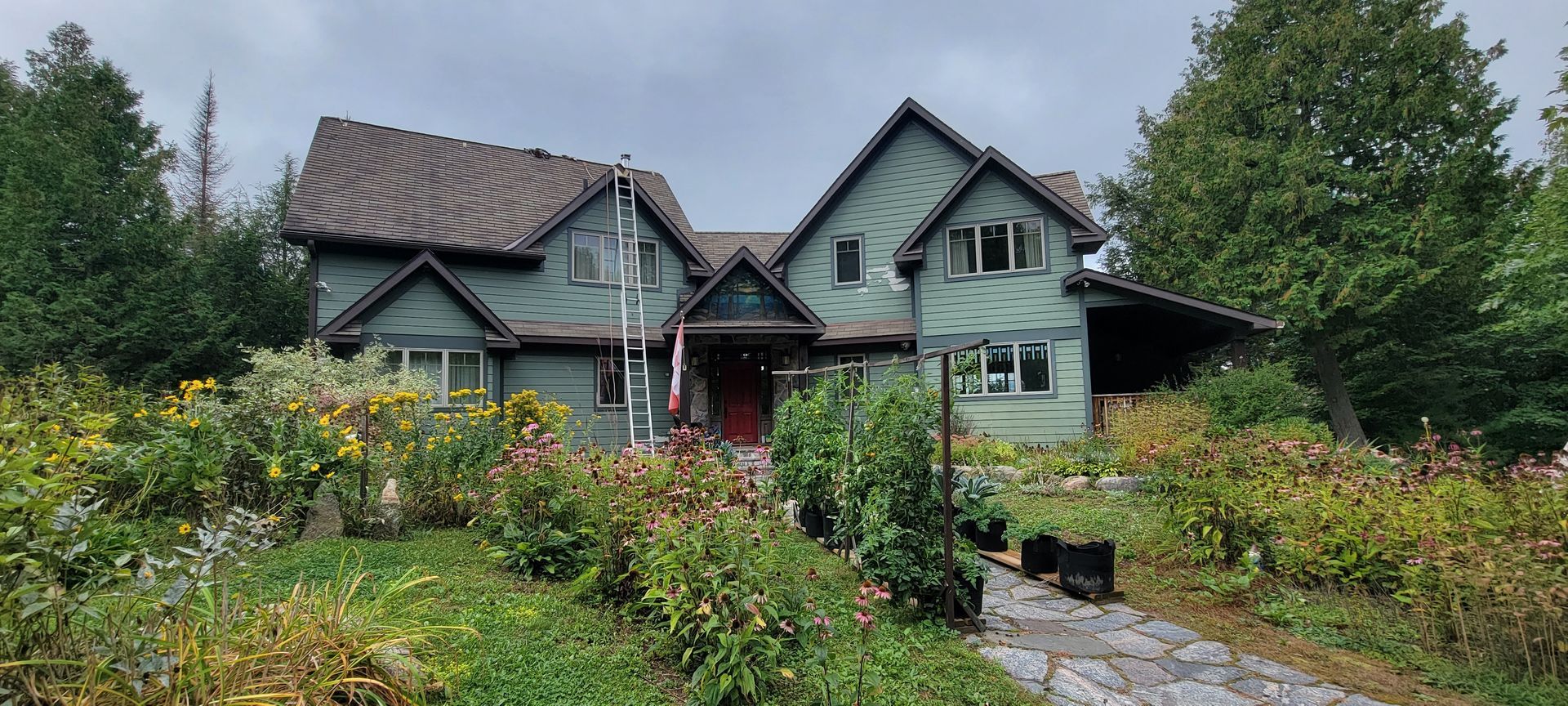 A large green house with a brown roof is surrounded by trees and bushes.