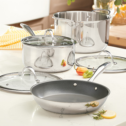 Stainless steel pots and frying pan on a white kitchen counter with spoons and lemon slices