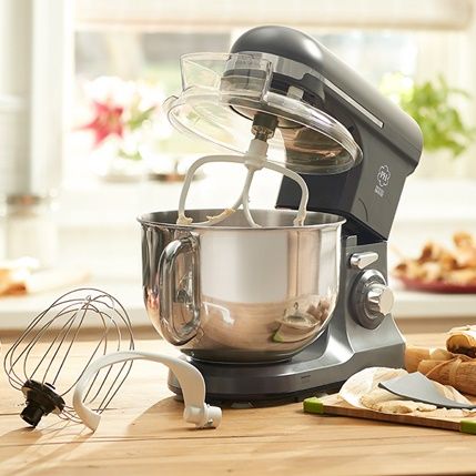 Stand mixer with stainless steel bowl and whisk attachment on a kitchen counter, with dough ingredients nearby