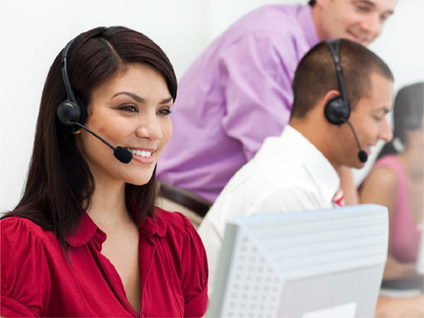 Call center staff wearing headsets at computers, with a smiling woman in the foreground