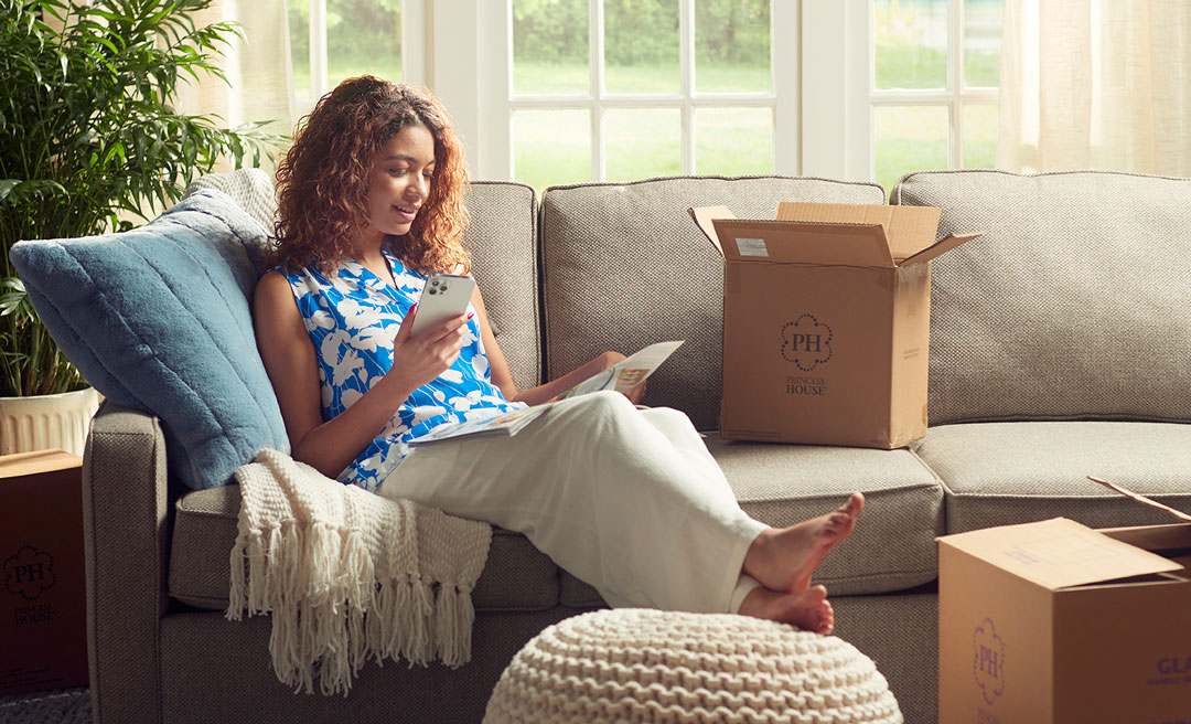 Person reading on a couch in a sunlit living room surrounded by moving boxes
