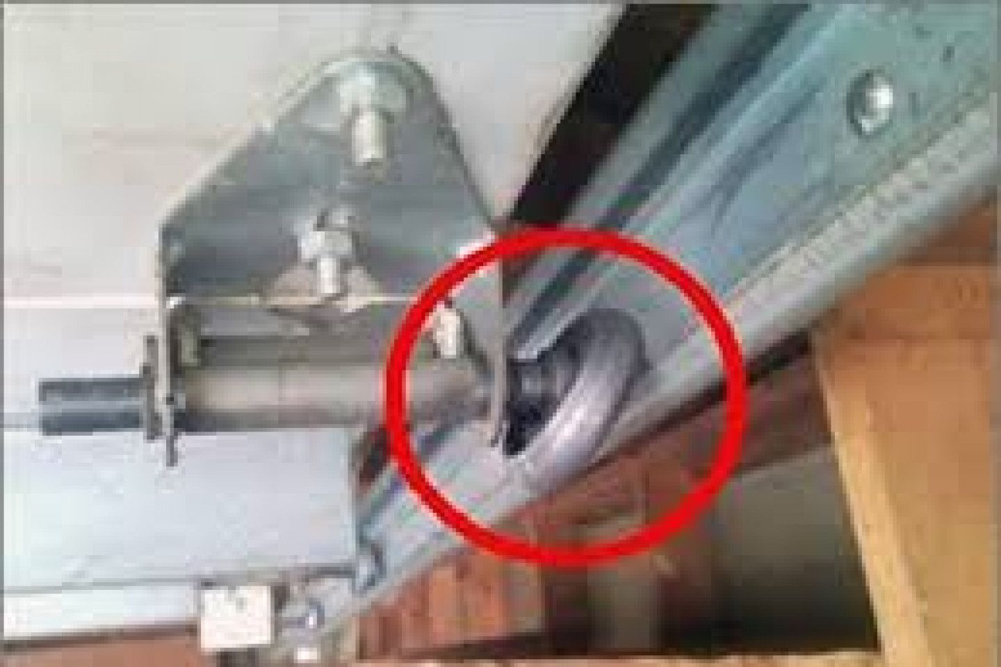Close-up of a garage door track and spring mechanism, with a red circle highlighting a bent metal part.