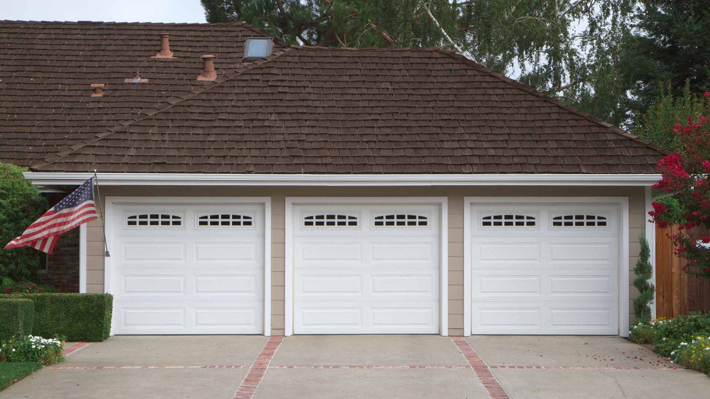 Three-car garage with white doors and an American flag on the left side of a suburban home.