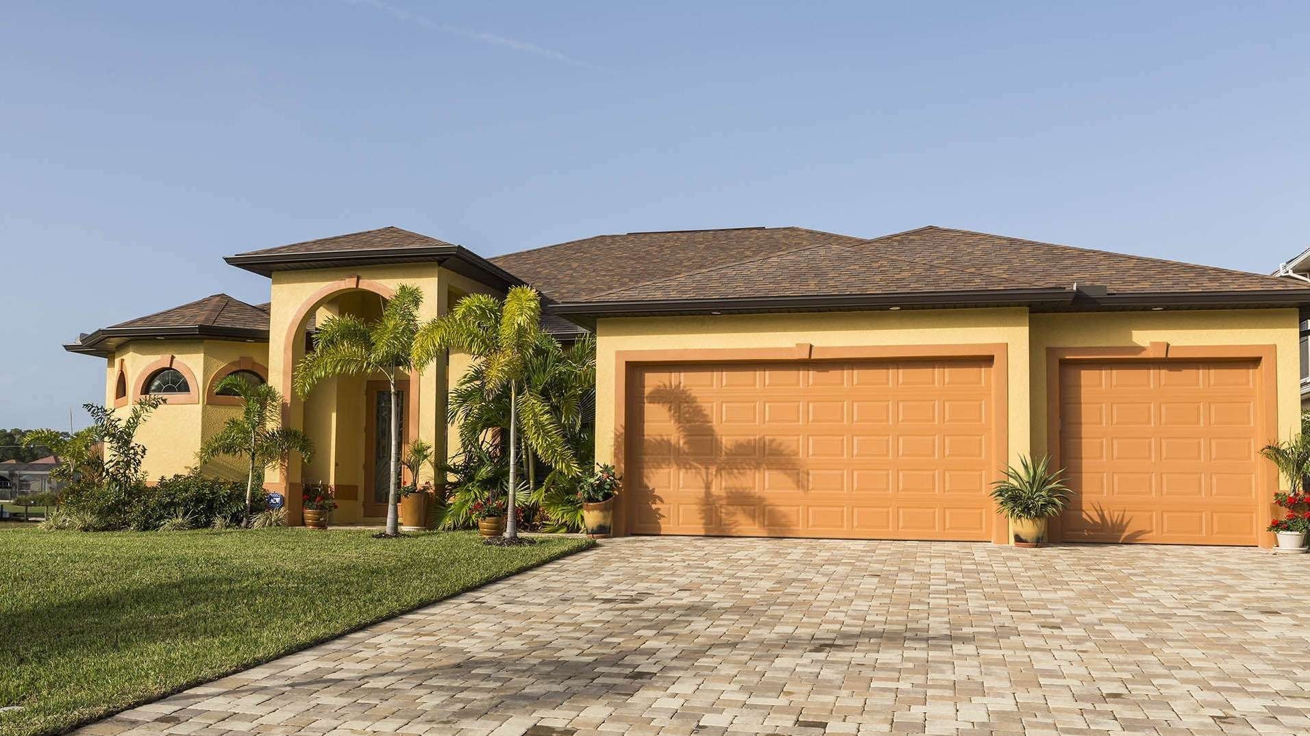 Single-story house with orange garage doors, stone driveway, and landscaped front yard in warm sunlight