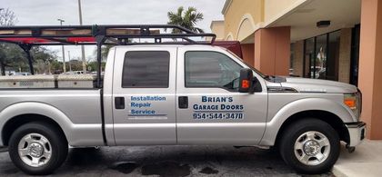 Silver pickup truck with business decals parked beside a building.