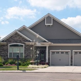 Suburban house with gray siding, stone accents, and a two-car garage under a blue sky