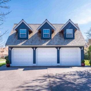 Suburban house with three white garage doors and three dormer windows under a blue sky