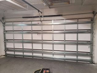 Large industrial garage door in a concrete garage, with a remote opener on the floor.