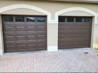 Two brown garage doors under beige arched stucco on a brick driveway