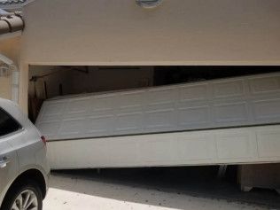A garage door bent upward with a silver SUV trapped beneath it in a residential driveway.
