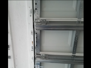 Interior of a metal cabinet with gray shelves and mounting rails, shown close up.