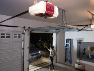 Person standing in an open garage doorway, reaching toward the garage door opener.
