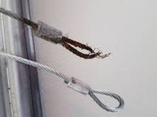 Two hanging metal cables, one frayed and rusted, against a light wall