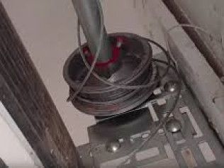 Broken metal wheel or pulley assembly with a cable on a gray floor.