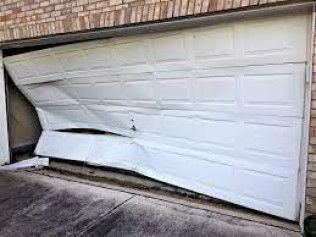 Collapsed white garage door bent inward under a brick house.