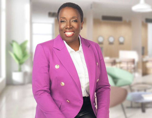 Photo of dr. judith josiah-martin sitting in an office lobby wearing a purple suit jacket and white shirt, smiling