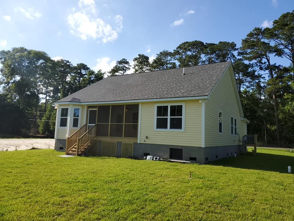 A pale yellow house with a gray shingled roof, a screened-in back porch, and stairs, set in a sunny, grassy backyard.
