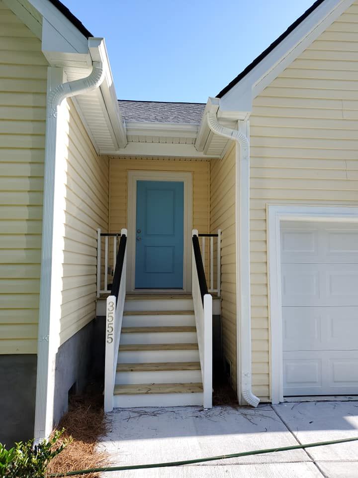 A pale yellow house with a light blue front door at the top of a short wooden staircase with white railings.