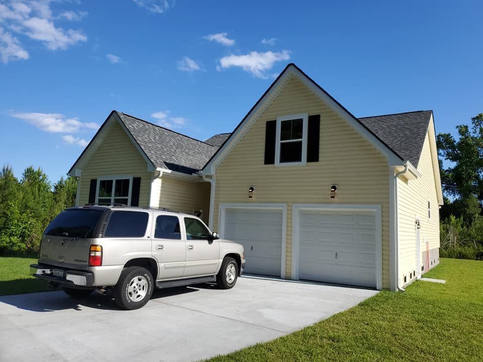 A light yellow, two-story suburban house with a two-car garage and a silver SUV parked on the concrete driveway.
