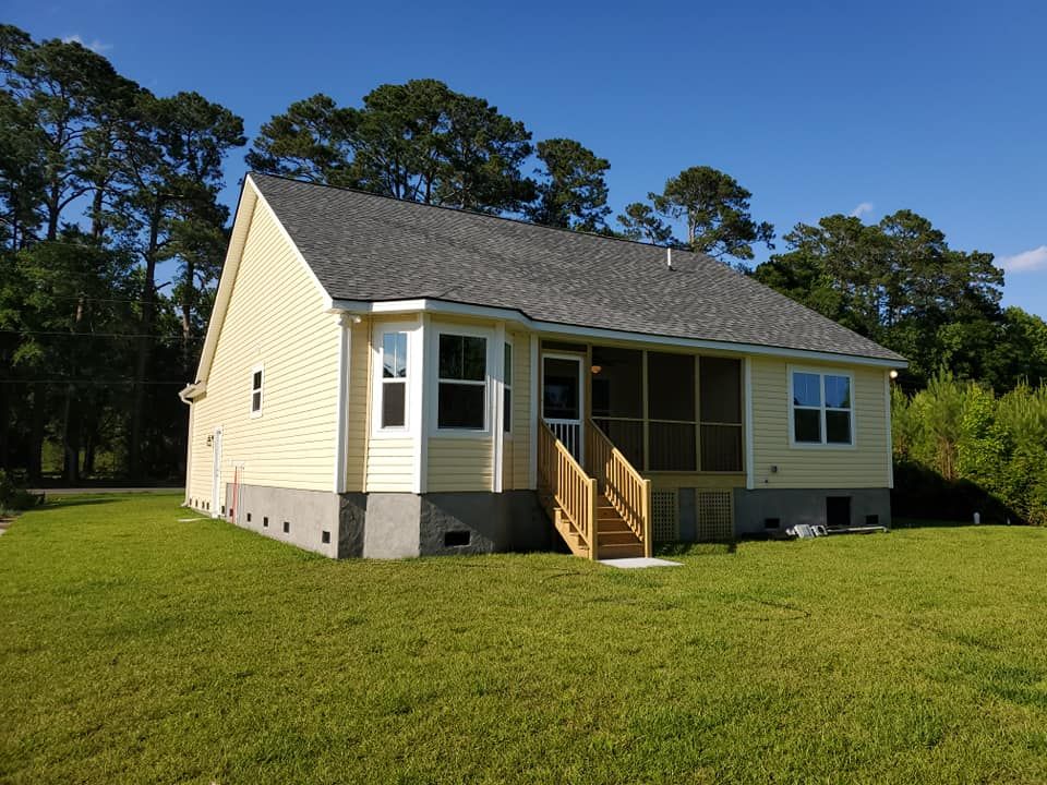 A yellow, single-story house with a screened-in porch, wooden stairs, and a grey shingled roof on a grassy lot.