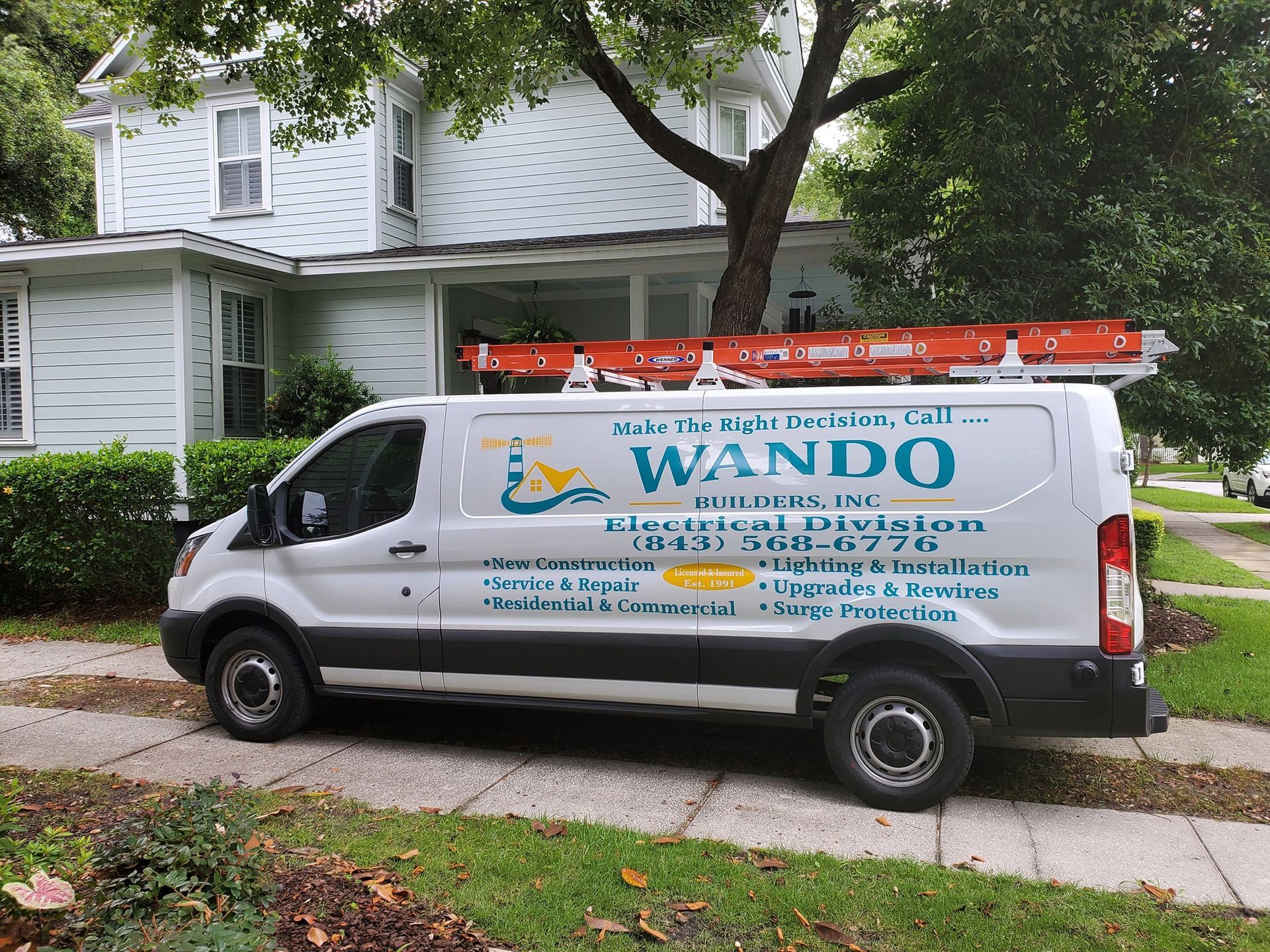 A white Wando Electrical Division work van parked on a residential driveway in front of a white two-story house.