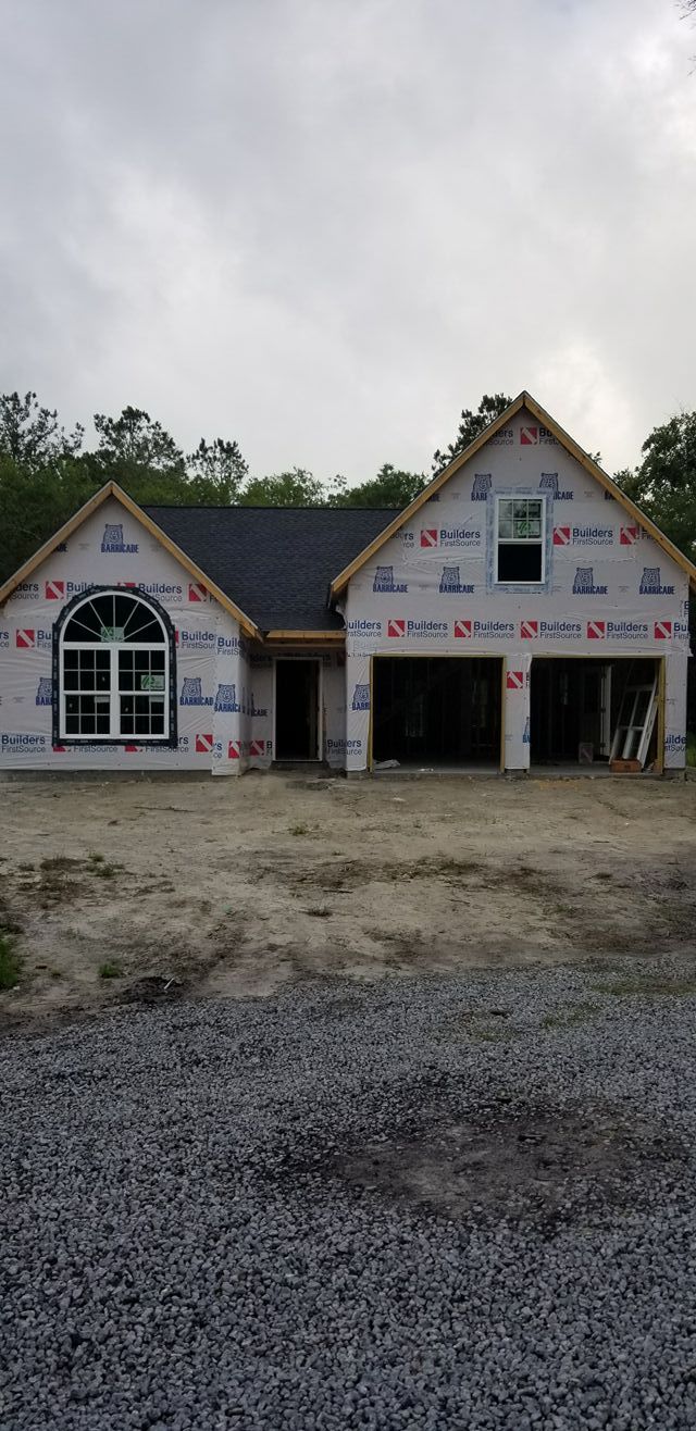A new residential house under construction, with exposed white house wrap and a gravel driveway in front.