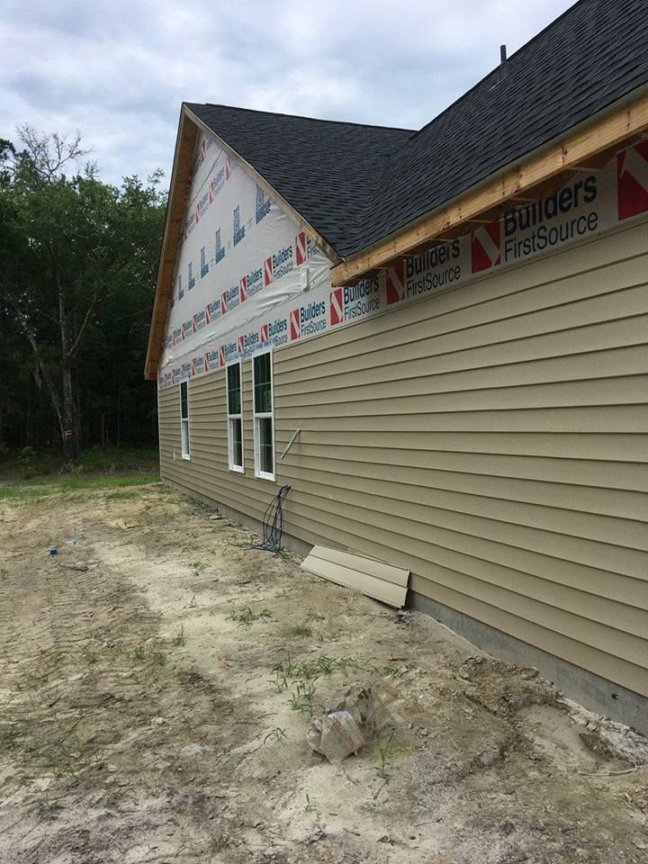 Side view of a new house under construction with tan horizontal vinyl siding and white-trimmed windows.