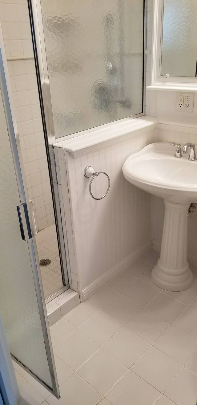 A white pedestal sink beside a shower stall with a glass door and a towel ring on the wall in a bright bathroom.