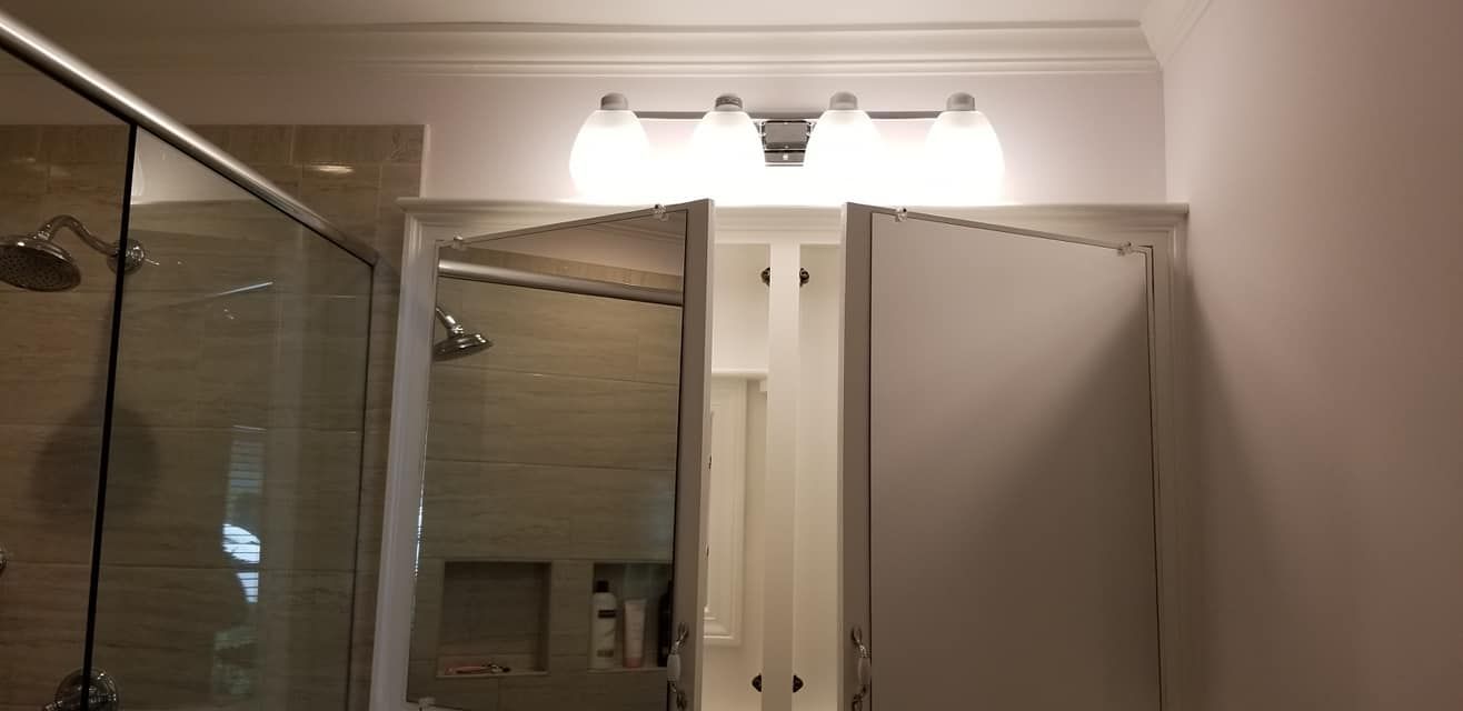 A bathroom vanity with a four-bulb light fixture above a mirror and a glass shower enclosure to the left.