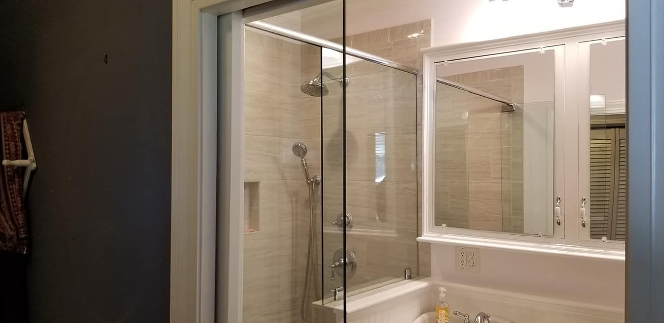 A modern bathroom featuring a glass-enclosed shower with tiled walls next to a vanity with a large white-framed mirror.