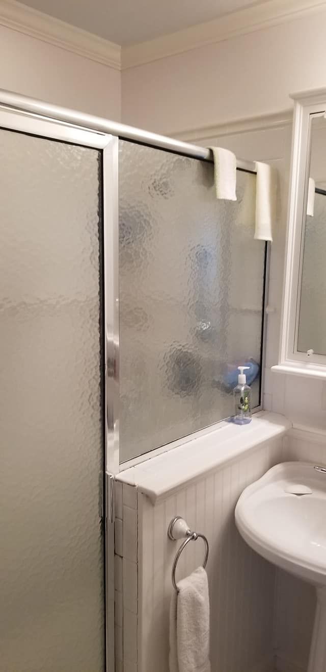 A bathroom featuring a glass shower enclosure with white trim, a small marble shelf, and a pedestal sink with a towel.