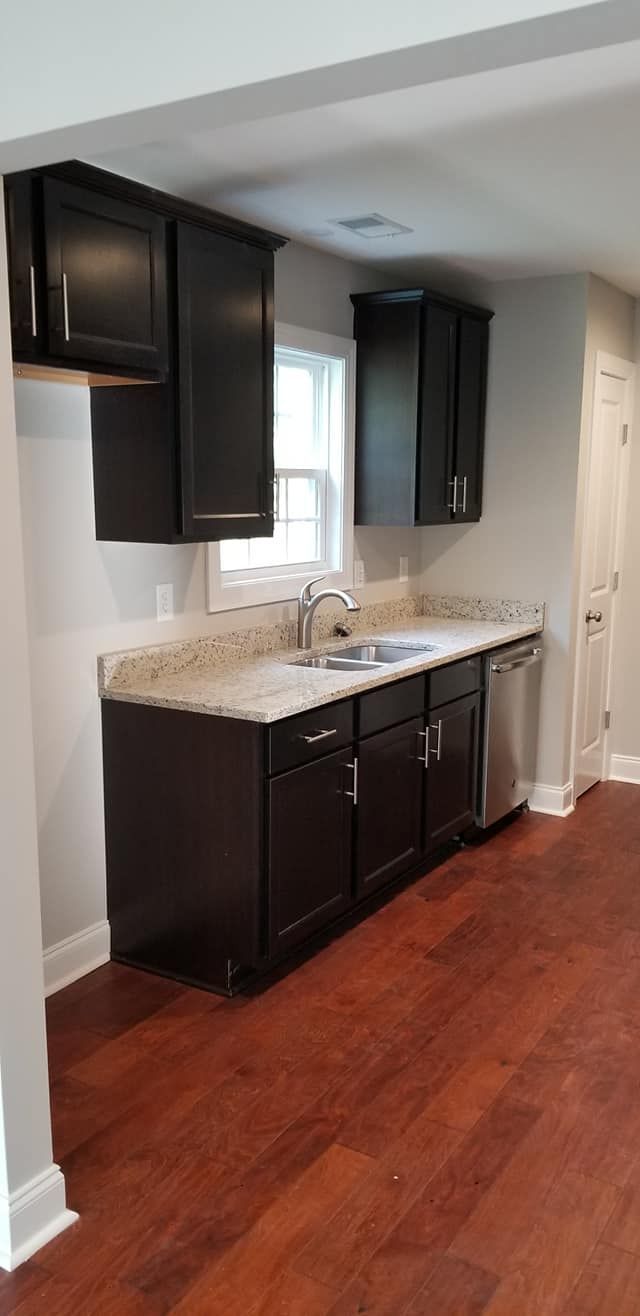 A kitchen counter with dark wood cabinets, light granite countertops, a stainless steel sink, and hardwood flooring.