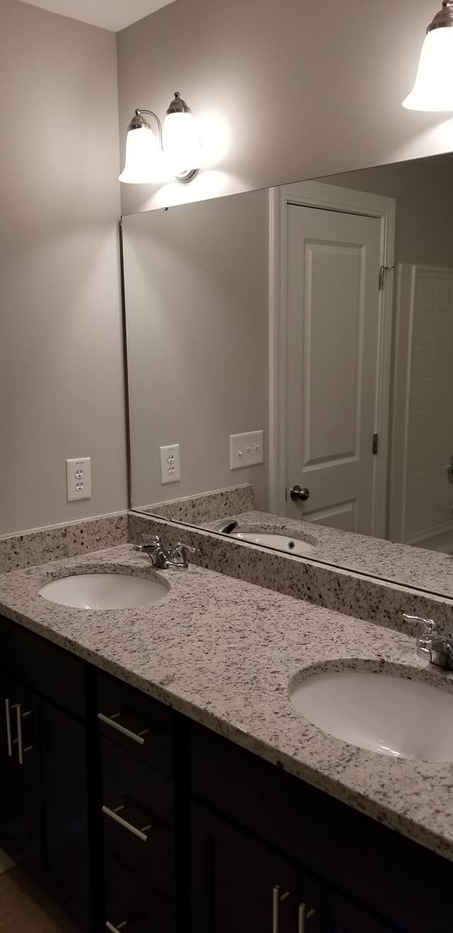 A dual-sink bathroom vanity with a speckled granite countertop, dark cabinets, and wall-mounted lights above a mirror.