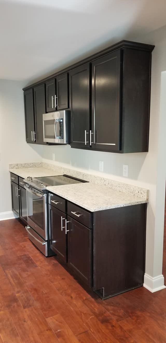 Modern kitchen featuring dark brown cabinetry, light granite countertops, stainless steel appliances, and hardwood floors.