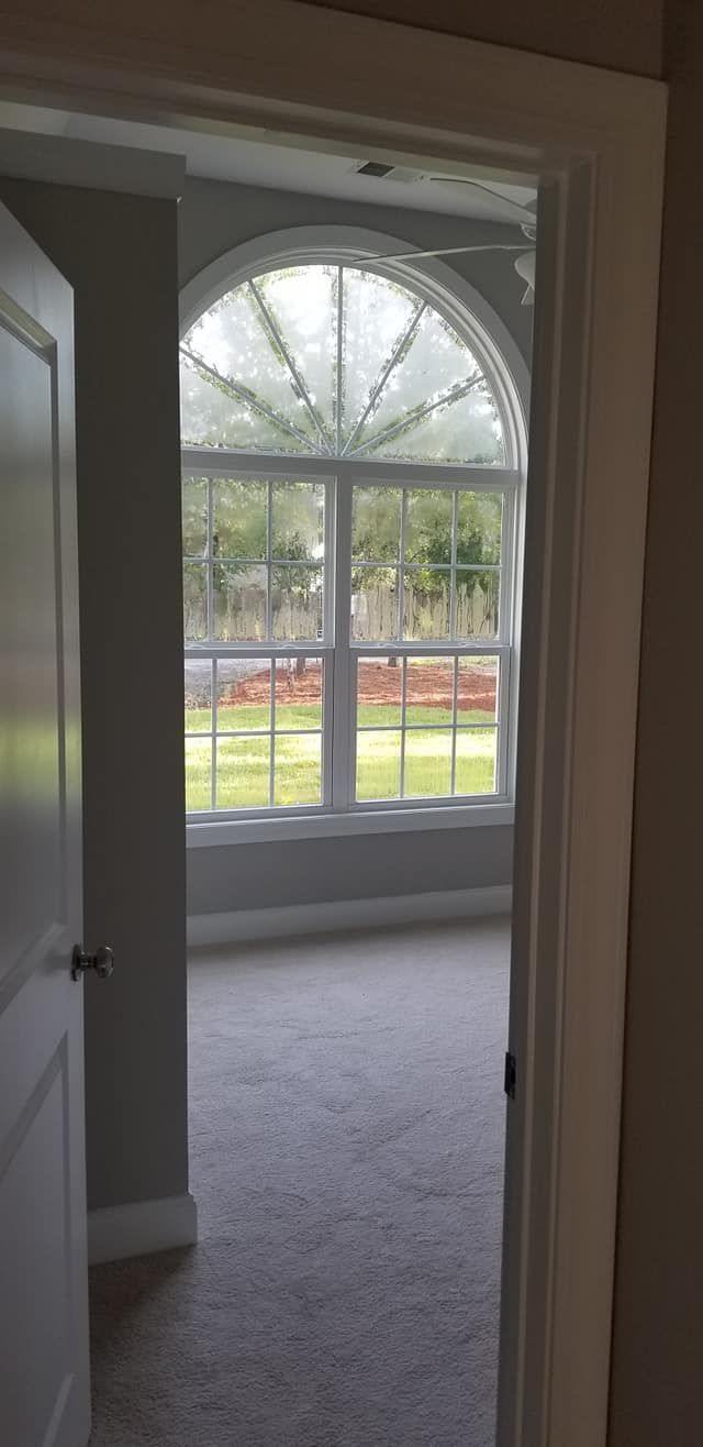 View through a doorway into a carpeted room featuring a large, arched window overlooking a grassy lawn.