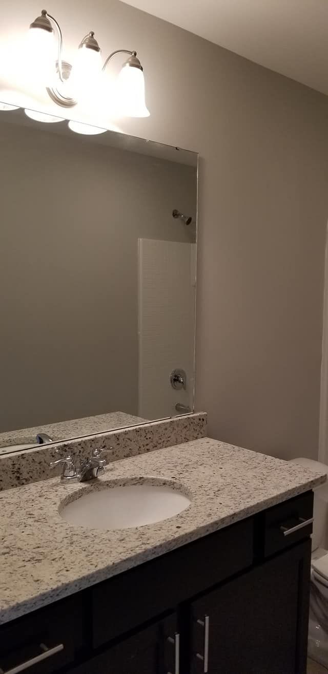 A bathroom vanity with a speckled granite countertop, white sink, dark cabinets, and a rectangular wall mirror.