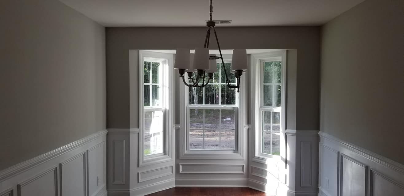 Dining room with beige walls, white wainscoting, and a bay window featuring a hanging chandelier above a wood floor.