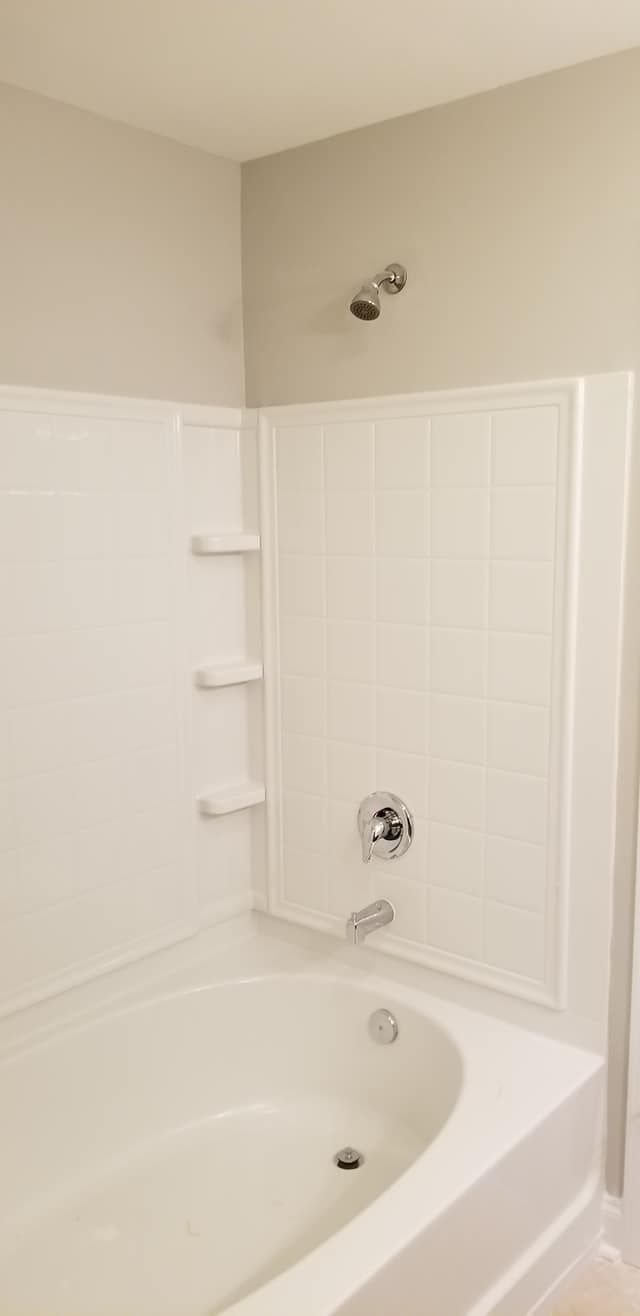 A white bathtub with a wall-mounted shower head, chrome faucet, and three built-in shelves against beige walls.