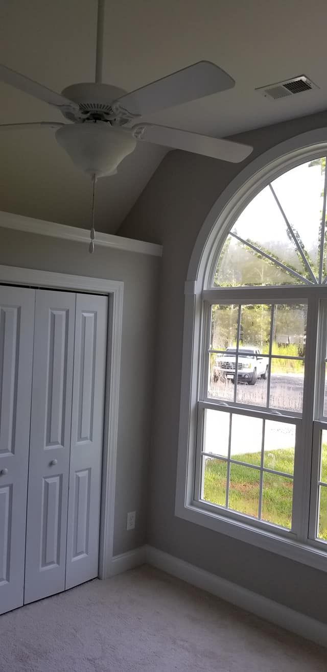 A room interior features a white ceiling fan, a large arched window with a view of a street, and a closed white closet.