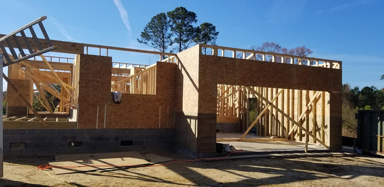 A residential house under construction, showing wood framing and plywood exterior walls on a concrete block foundation.