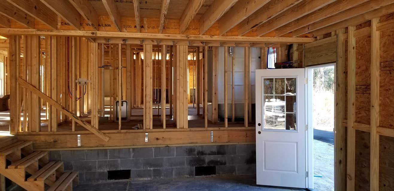 Framed walls of a building under construction, featuring wooden joists, concrete block foundation, and an open doorway.